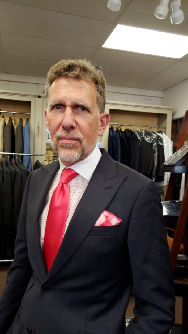 A man in a suit and tie standing next to a rack of suits.